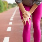 osteoartrosi. Female jogger wearing pink tights, injuring knee. Closeup of female hand holding leg. Athletic injury concept