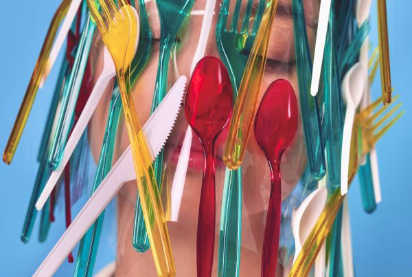 Microplastiche: una donna con forchette di plastica colorate intorno al volto