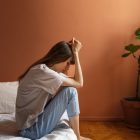 Distimia o depressione: ragazza seduta sul letto di lato con le mani sulla testa