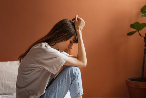 Distimia o depressione: ragazza seduta sul letto di lato con le mani sulla testa